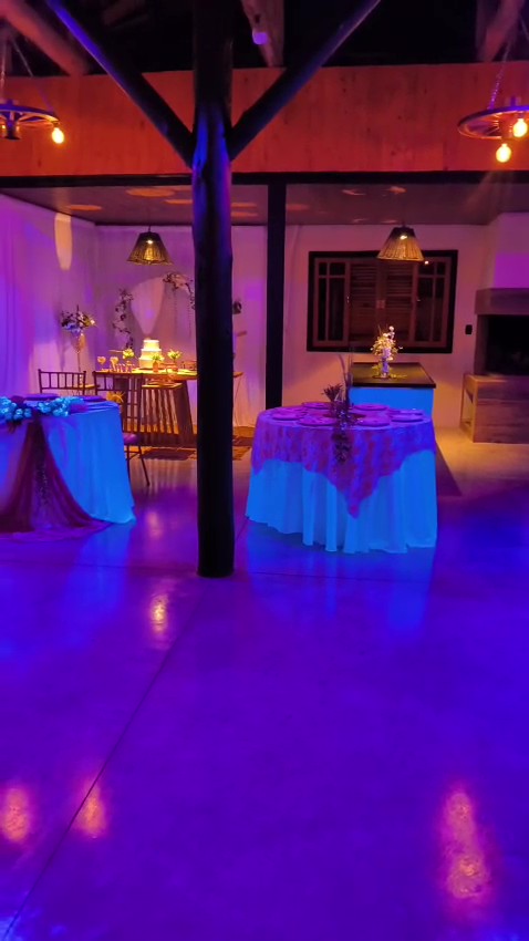 Salão decorado com iluminação cênica e mesa do bolo ao fundo